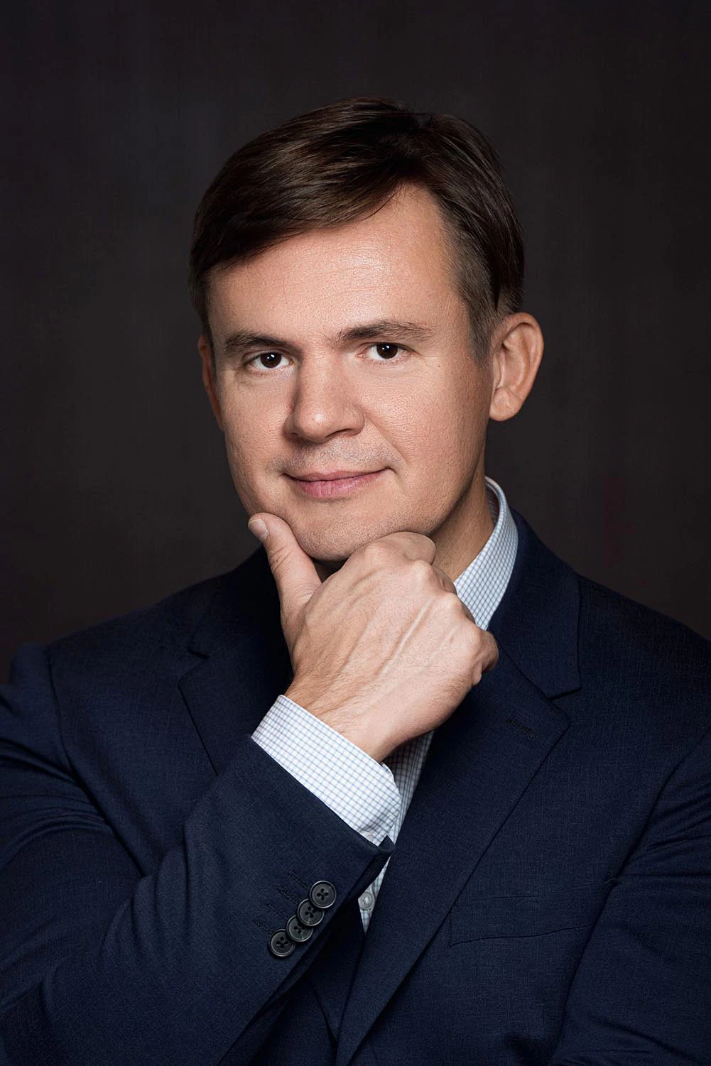 Крупный план имиджевого портрета мужчины в тёмно-синем костюме с рукой у подбородка. Профессиональная бизнес-съёмка на тёмном фоне, Москва